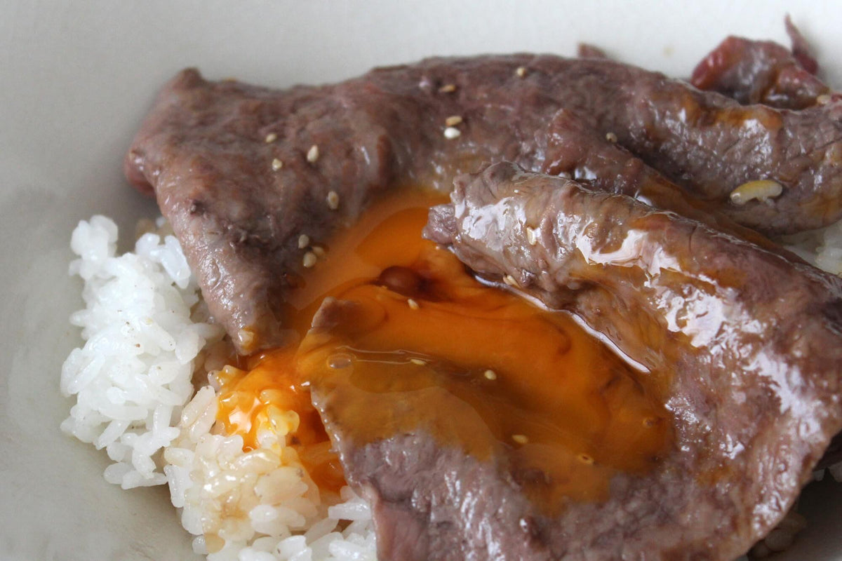 マーブラン 黒毛和牛の赤身スライス肉 丼に盛りつけた白ご飯の上に大判の焼いたお肉を載せ、卵黄をかけた贅沢牛丼
